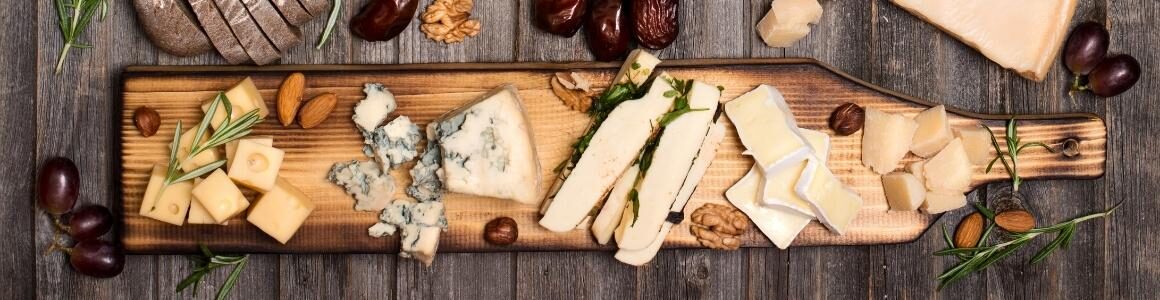 A variety of cheeses, nuts, bread and herbs displayed on a wooden platter.
