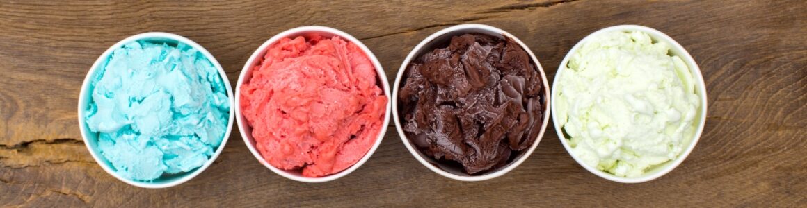 A variety of colorful ice creamed lined up in bowls with a wooden background.