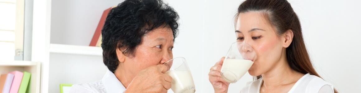 Two women drinking white dairy milk from clear mugs.