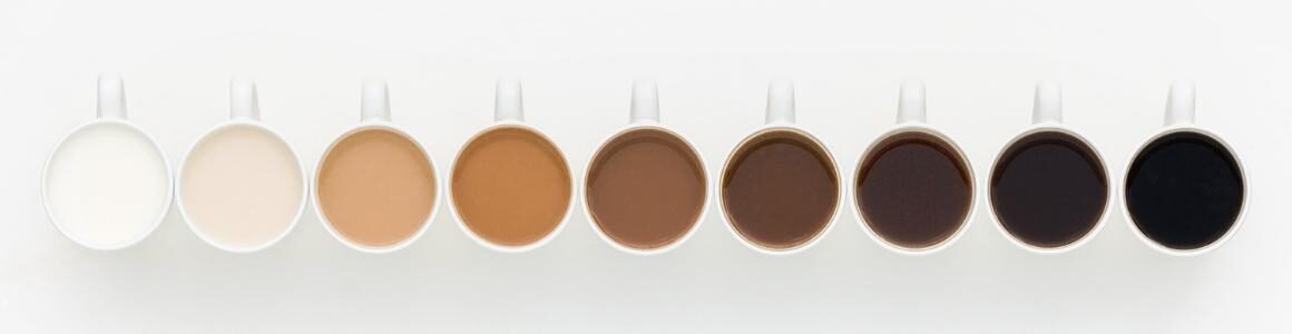 A row of white coffee mugs with light and dark coffee displaying amount of creamers used.